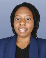 Rebecca, smiling on a blue/gray background, wearing a Navy blazer and a black shirt